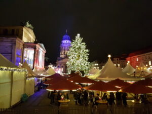 Blick von oben auf den Weihnachtszauber am Gendarmenmarkt mit den weißen Zelten, dem Weihnachtsbaum und dem Französischen Dom im Hintergrund